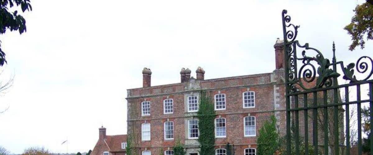A large brick building with a gated entrance, parked cars, and a grassy area with fallen leaves.