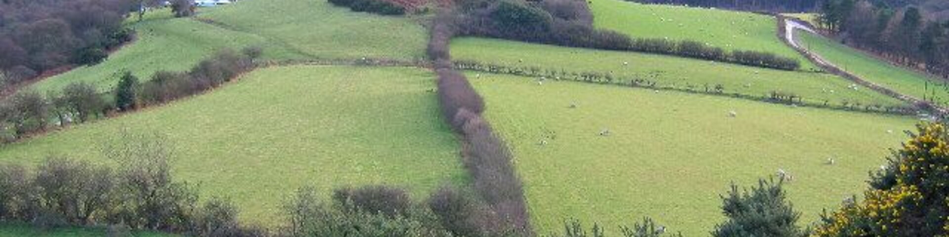 Colinas verdes ondulantes, uma estrada sinuosa e uma pequena aldeia no vale.