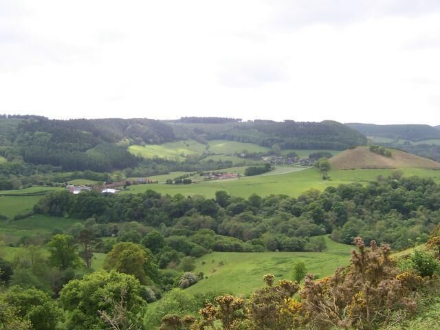 Rolling hills, green fields, and scattered houses in a rural landscape.