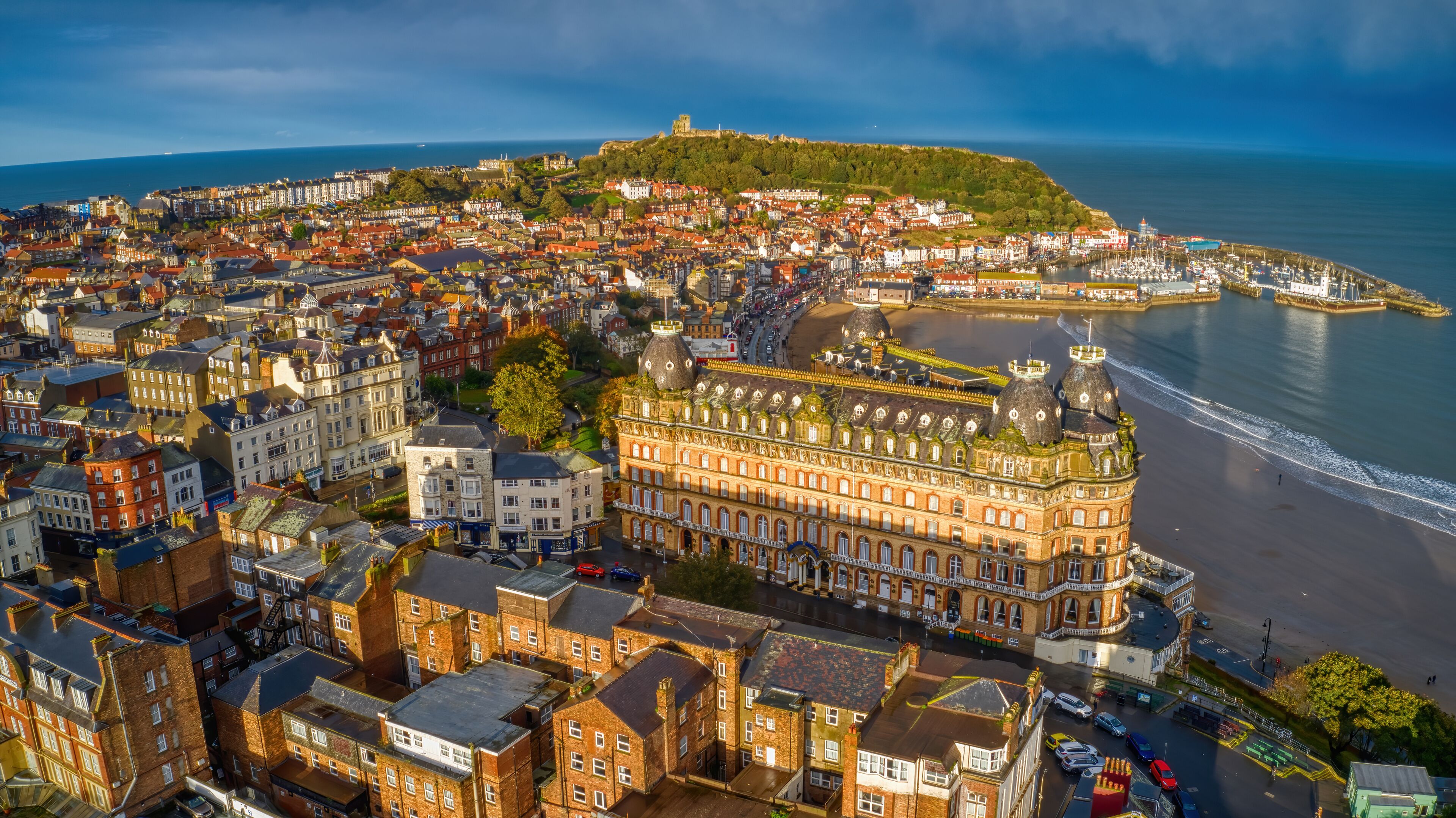 Paisagem costeira urbana com edifícios históricos, um castelo imponente numa colina e um porto de recreio.