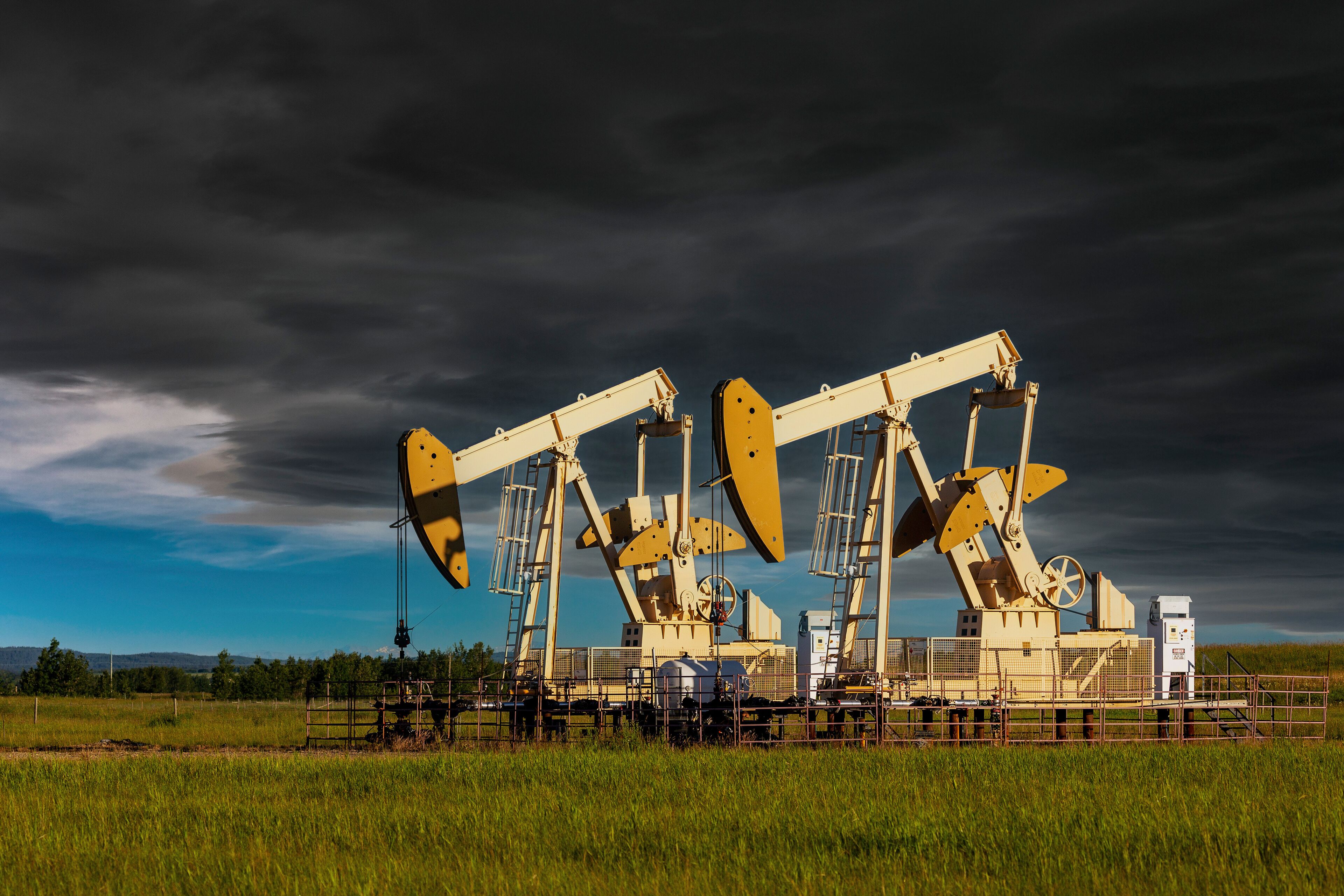 Two yellow pumpjacks in a green field with storm clouds in a dramatic dark sky, West of Airdrie; Alberta, Canada