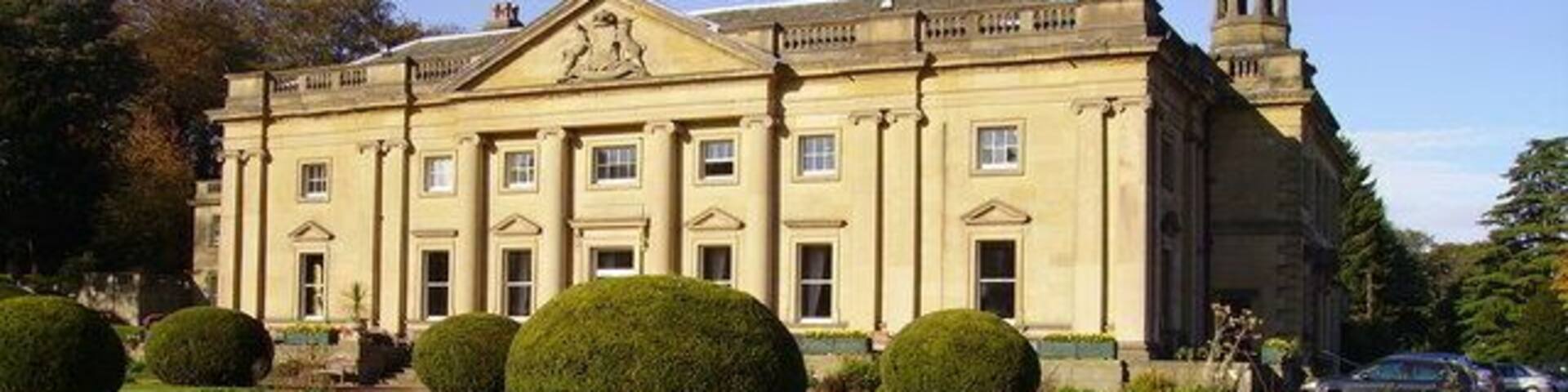 A large stately building with a symmetrical facade, surrounded by well-manicured lawns and topiary.