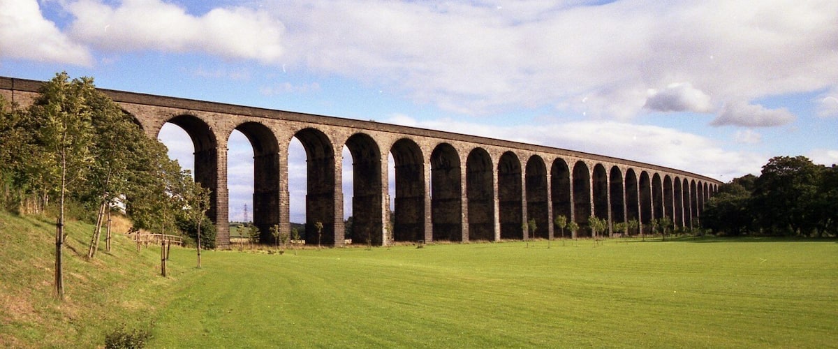 A long viaduct with multiple arches over a grassy field.