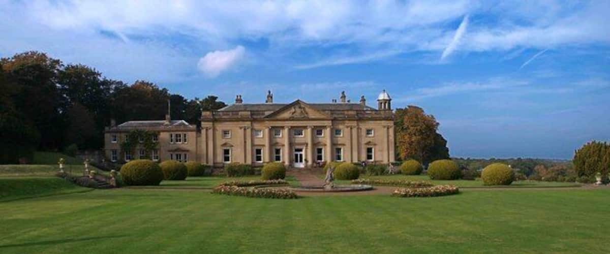 A large, historic building with a symmetrical facade, surrounded by well-manicured lawns and formal gardens.