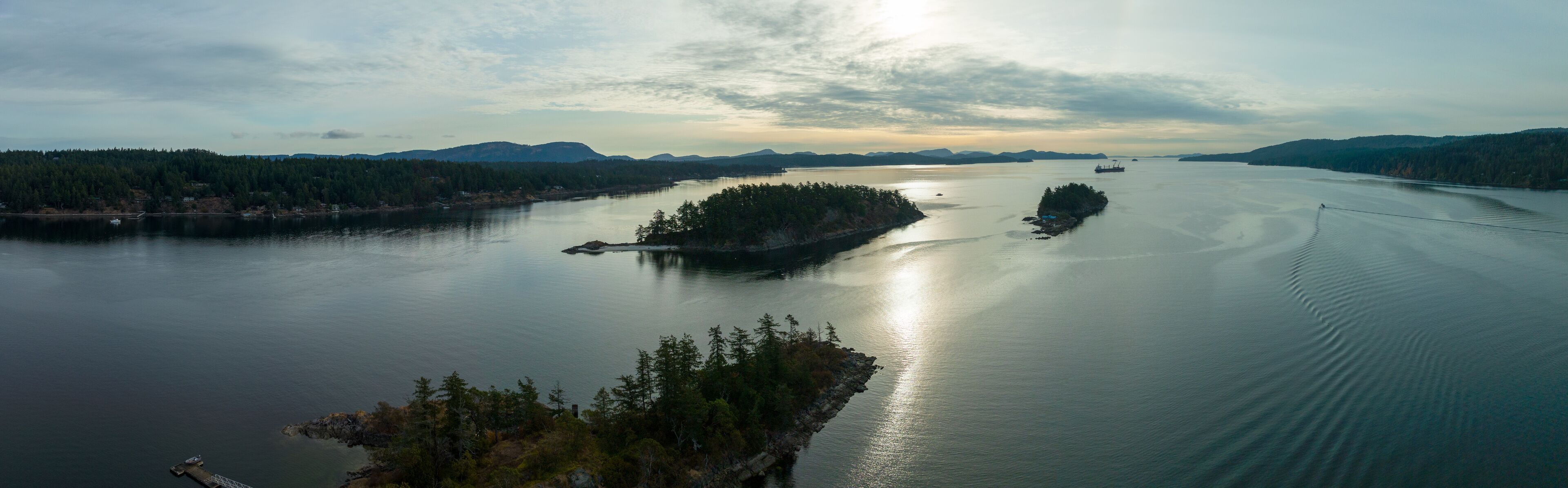 A calm lake with a small island in the center, surrounded by dense forests and distant mountains.