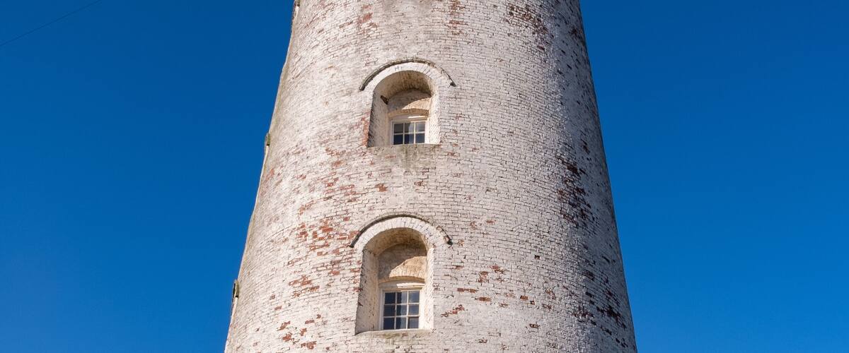 A tall brick lighthouse with arched windows and a door at the base.