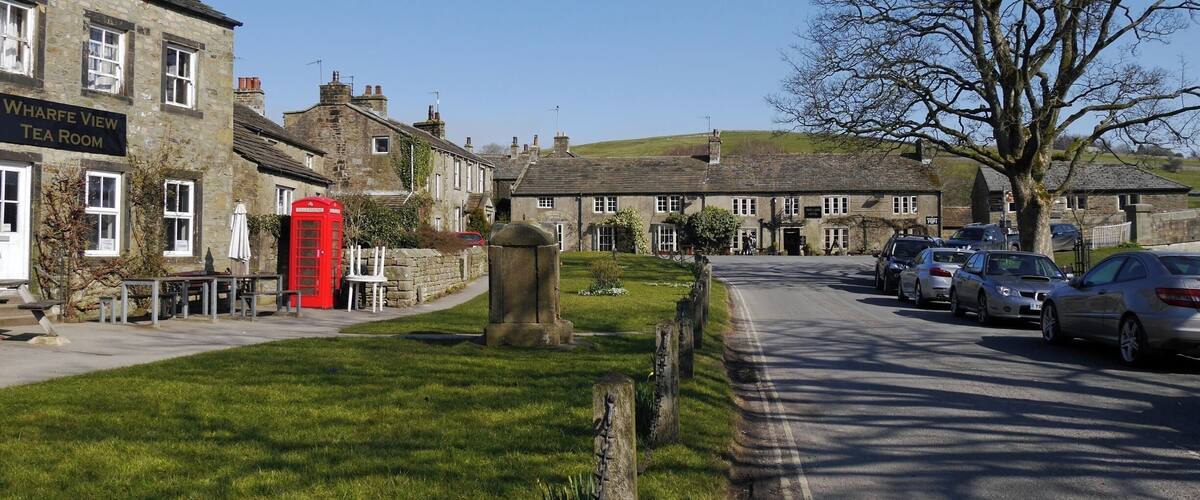 A quaint village street with stone buildings, a red telephone booth, and parked cars.