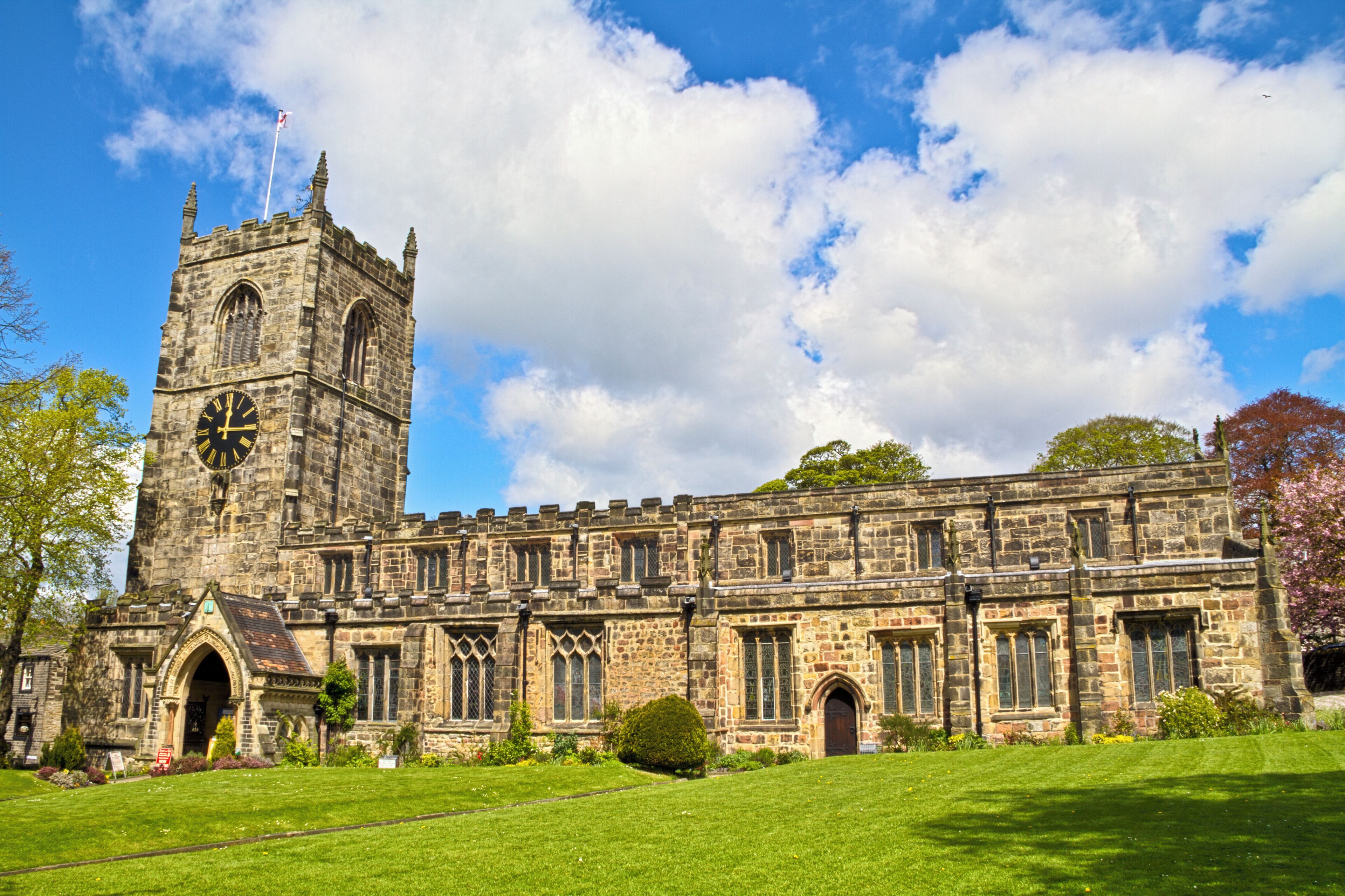 A historic stone building with a clock tower, arched windows, and a well-maintained lawn.
