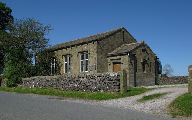A stone building with a sloped roof, a wooden door, and a stone wall.