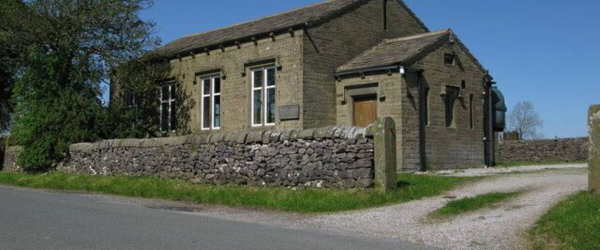 A stone building with a sloped roof, a wooden door, and a stone wall.