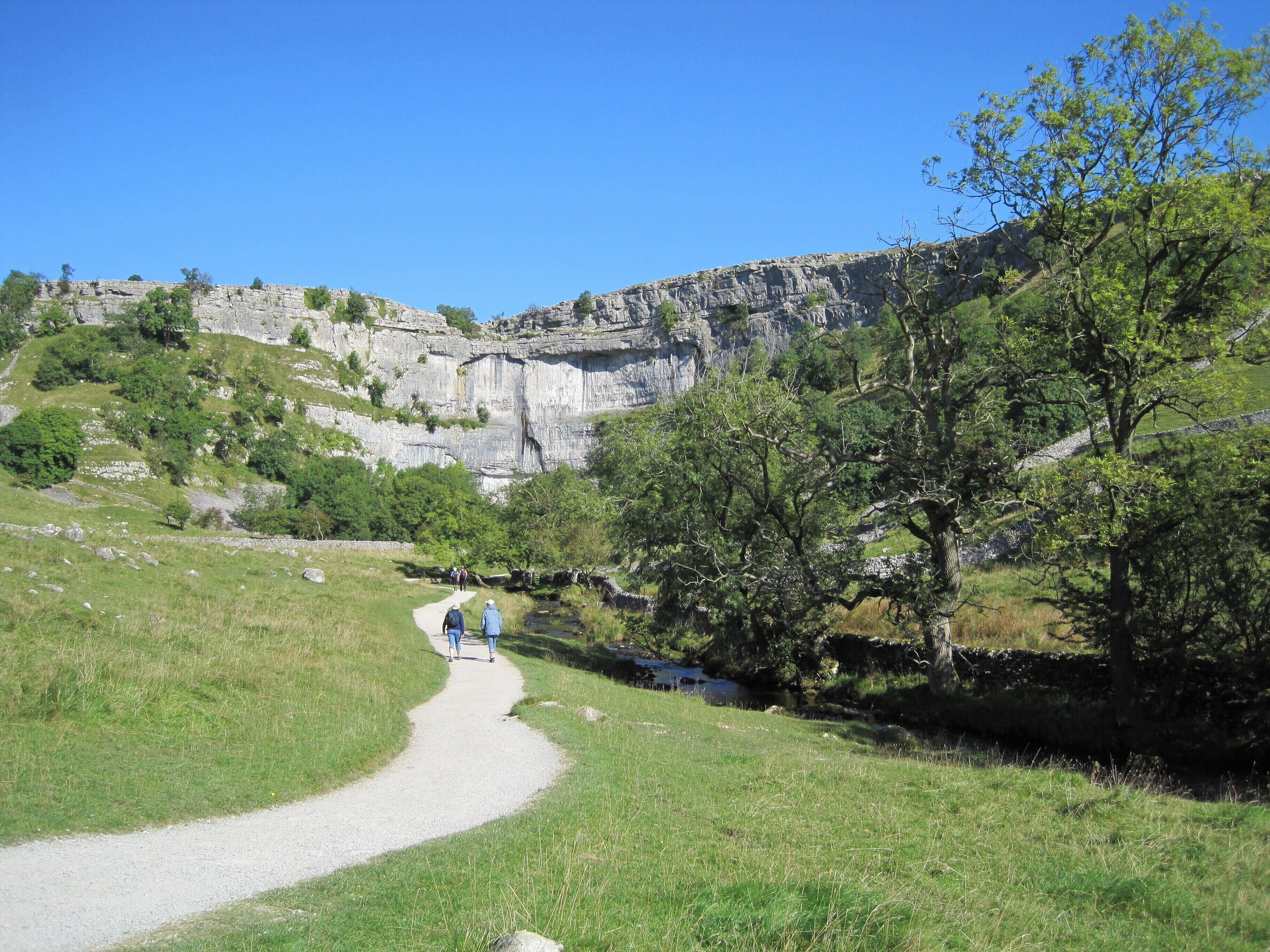 A gravel path winding through a grassy field with a rocky cliff in the background.
