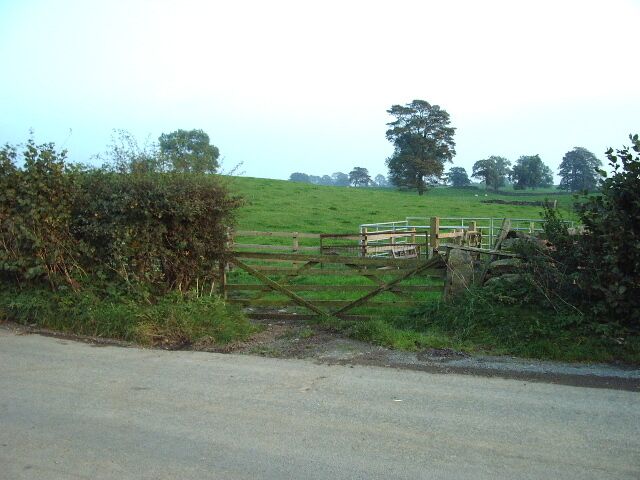 A rural road with a wooden gate leading to a fenced field.