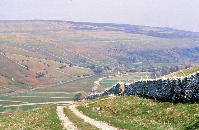 A rural landscape with rolling hills, a dirt path, and a stone wall.