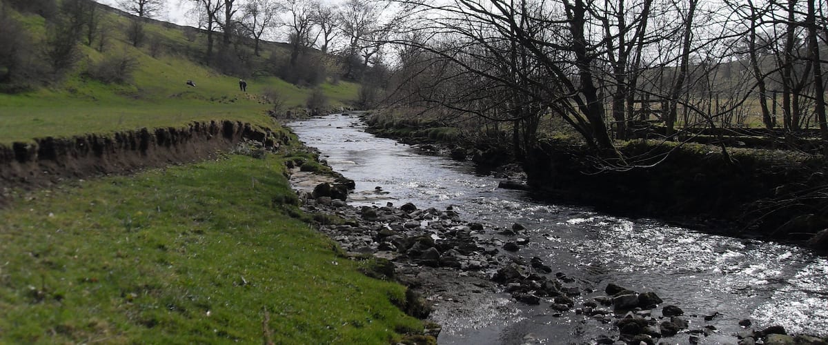 A river flowing through a valley with rocky banks and leafless trees.
