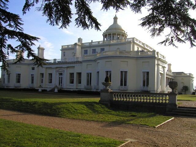 A large white building with a dome and columns, surrounded by a well-maintained lawn and a decorative fence.