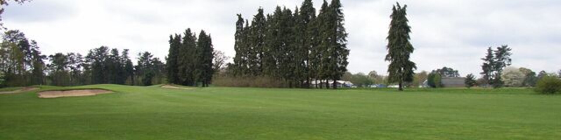 Un campo de golf con césped verde, bunkers de arena y altos árboles al fondo.