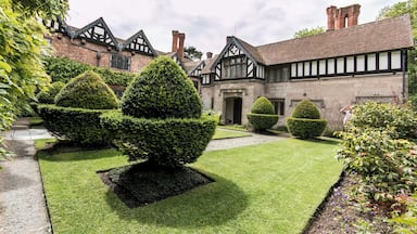 Un bâtiment de style Tudor doté d’un jardin bien entretenu, avec des haies taillées et un chemin pavé.