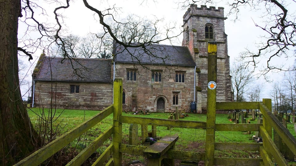 A stone church with a tower and a wooden gate in a cemetery.