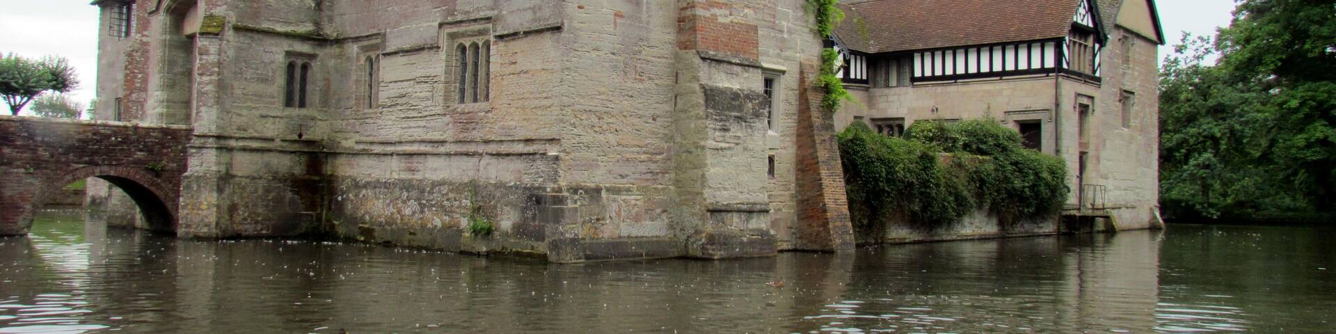 A historic building by a river with ducks swimming in the water.