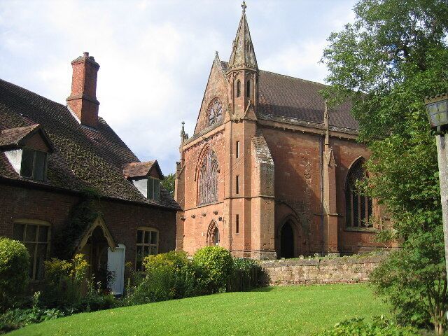 A historic church with a tall spire, brick walls, and a well-maintained lawn.
