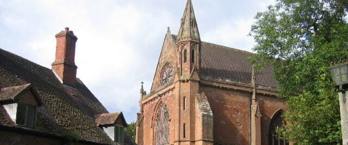 A historic church with a tall spire, brick walls, and a well-maintained lawn.