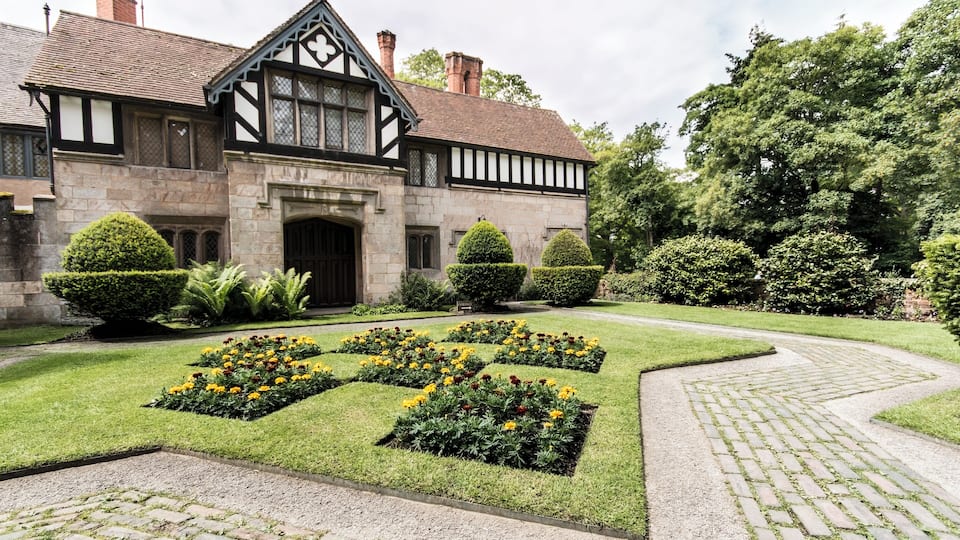 A Tudor-style building with a symmetrical garden featuring flower beds and trimmed hedges.