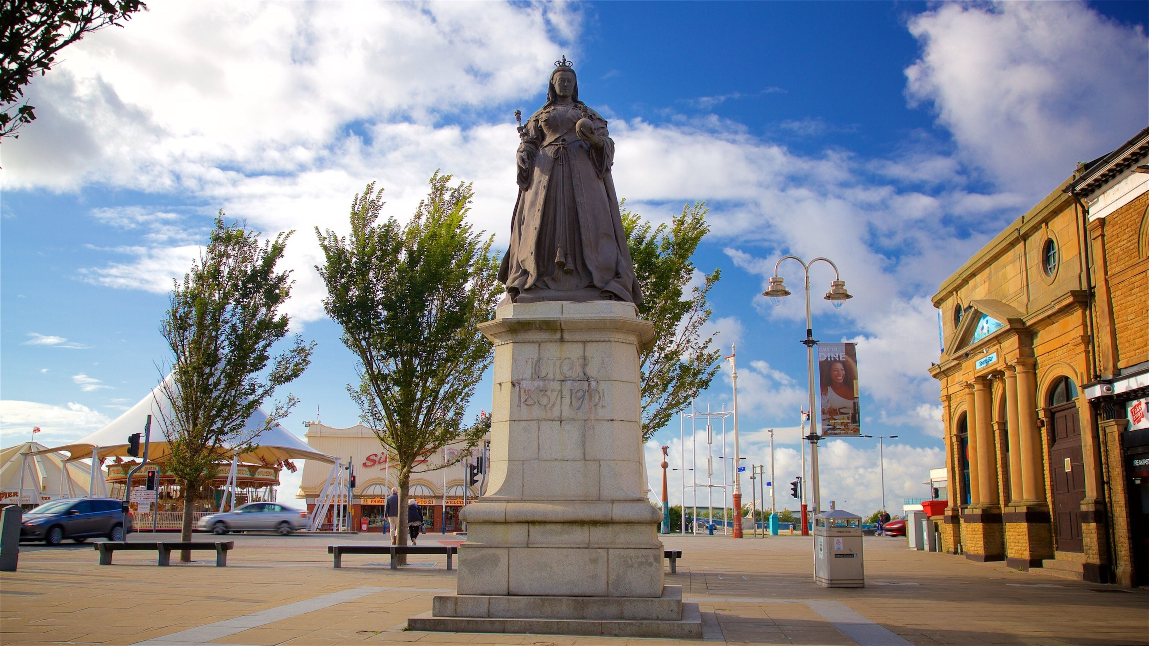 A statue of a woman on a pedestal with a clear sky and buildings in the background.