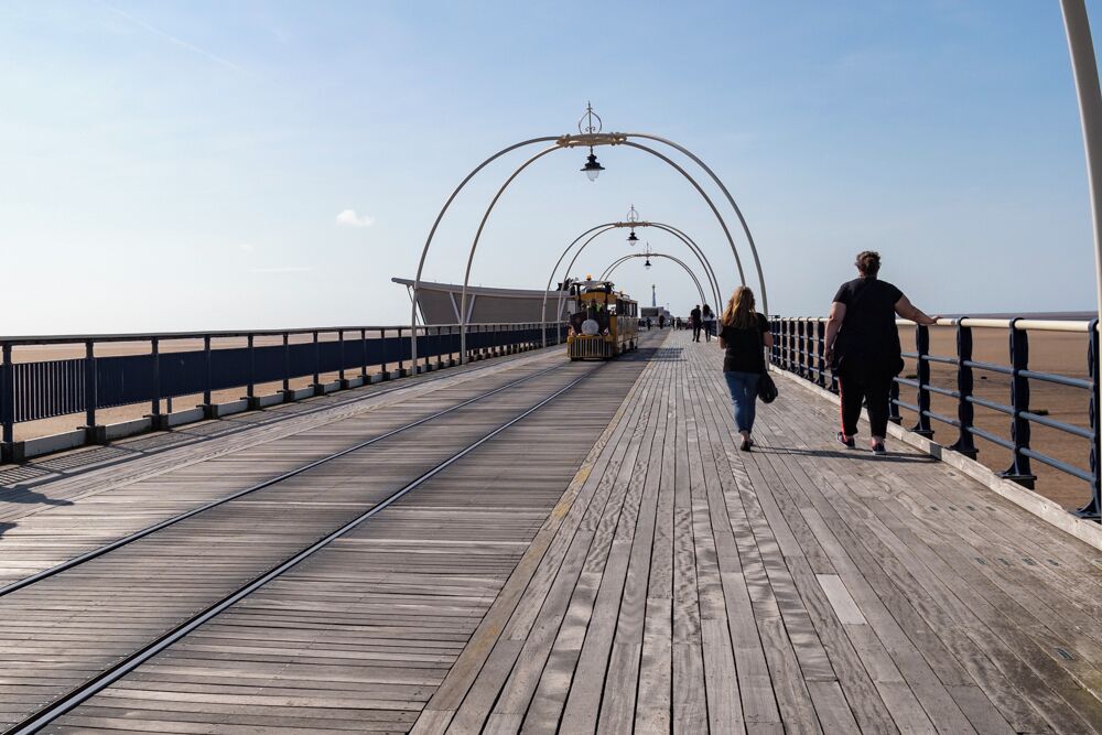 A wooden boardwalk with metal railings, a small train, and people walking.