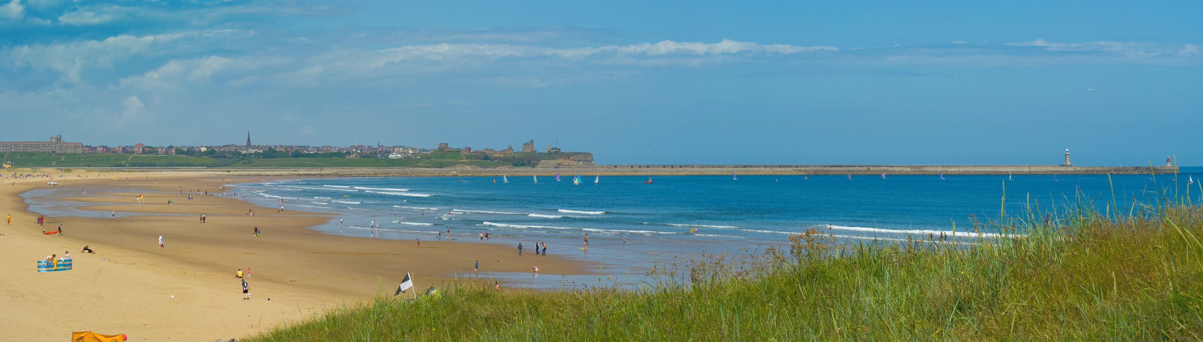 A beach with people, a lighthouse, and a castle in the background.