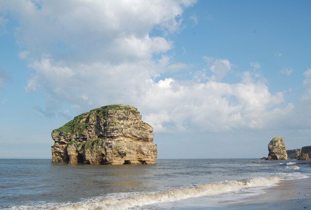 A coastal landscape with a prominent rock formation in the sea and a smaller rock in the background.