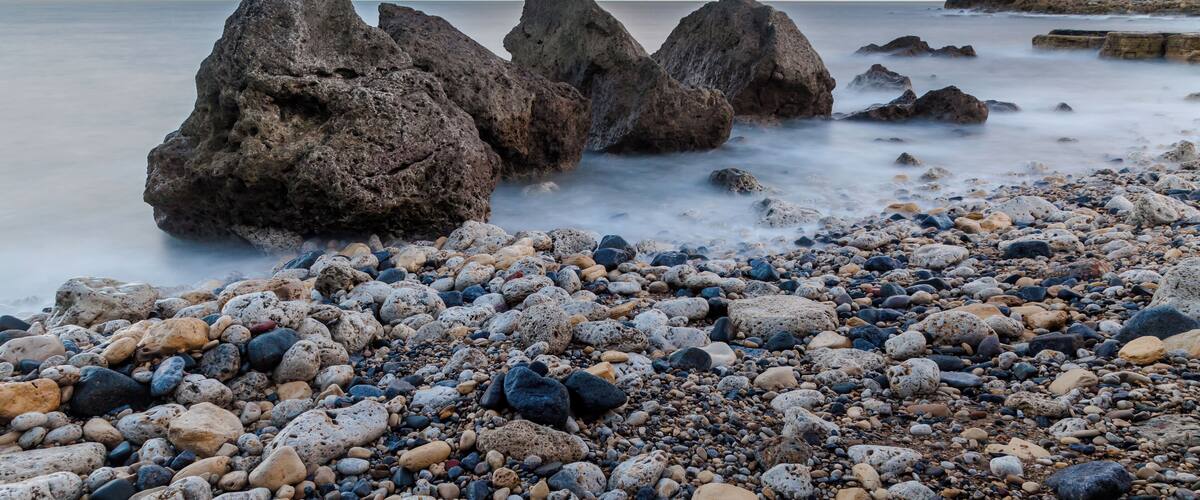 A rocky shoreline with large boulders and a pebbly foreground.