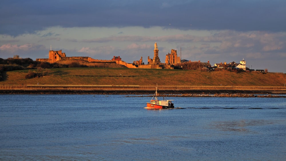 Une rivière avec un bateau, un château et une statue sur une colline.