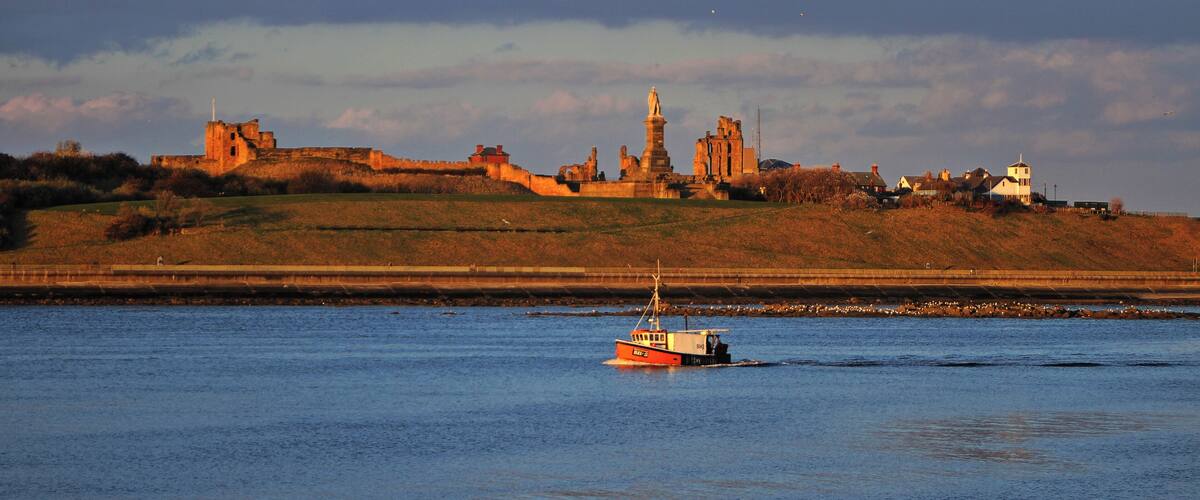 A river with a boat, a castle, and a statue on a hill.