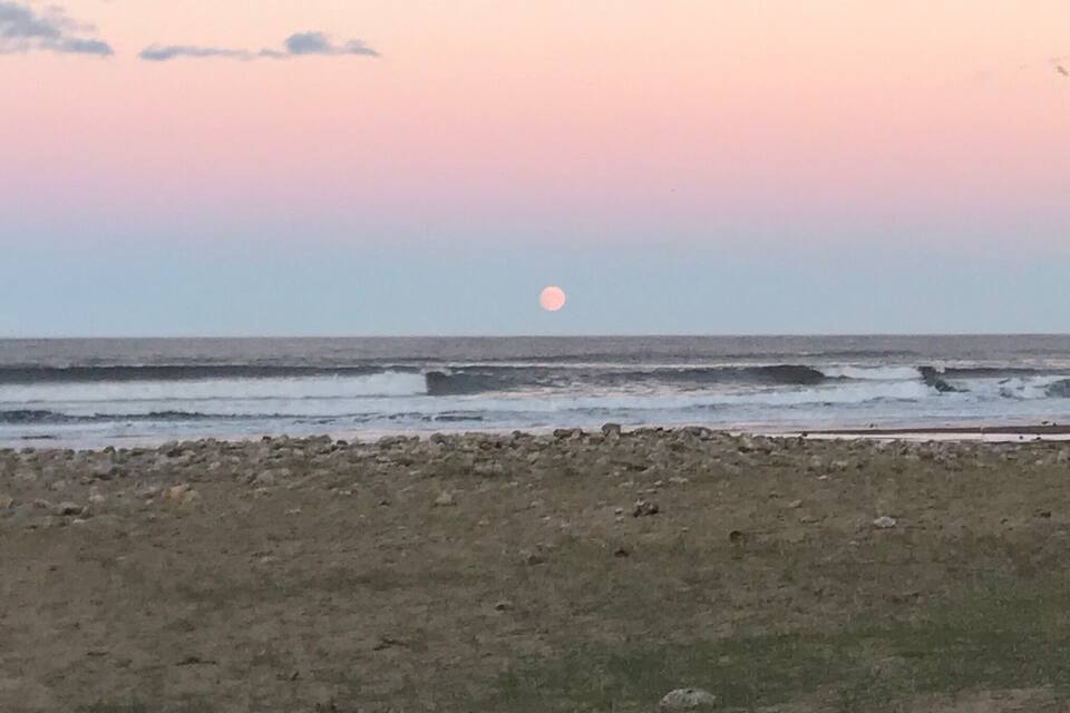 A beach with a rocky foreground and a sunset over the ocean.