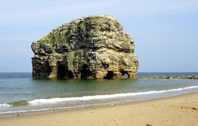 A large rock formation on a beach with calm waves.