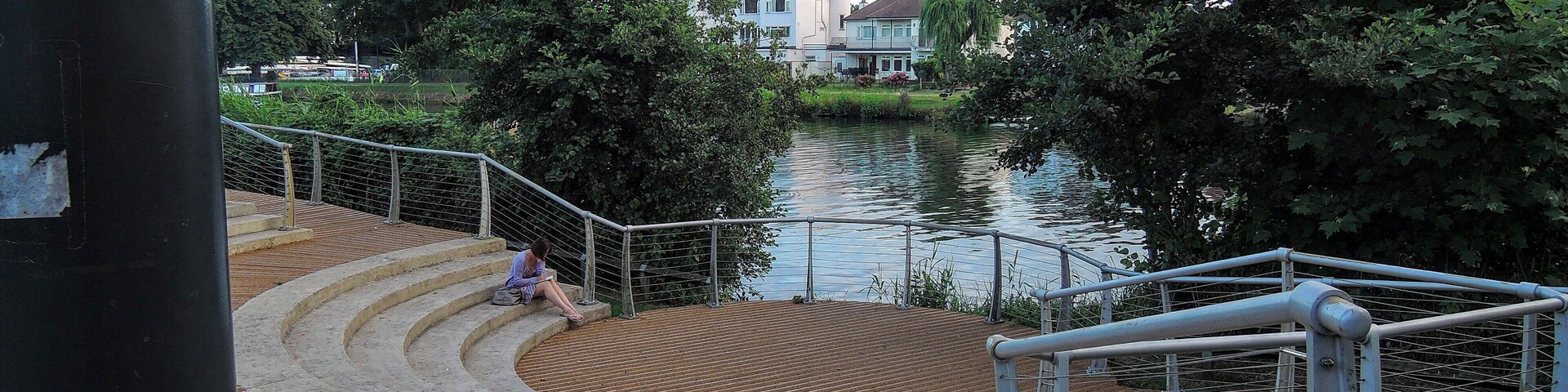 Un paseo ribereño con escaleras que bajan a una terraza de madera al borde del agua.