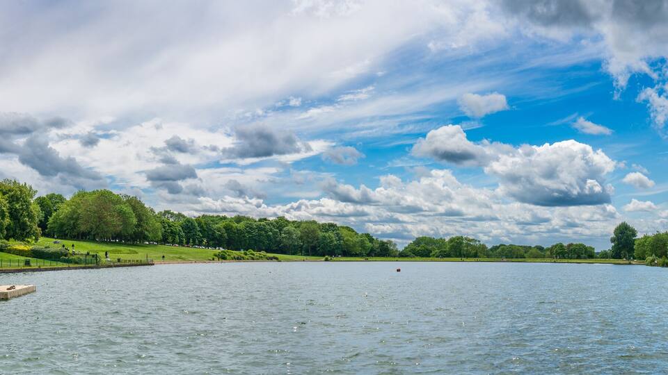 A calm lake surrounded by lush greenery and a partly cloudy sky.