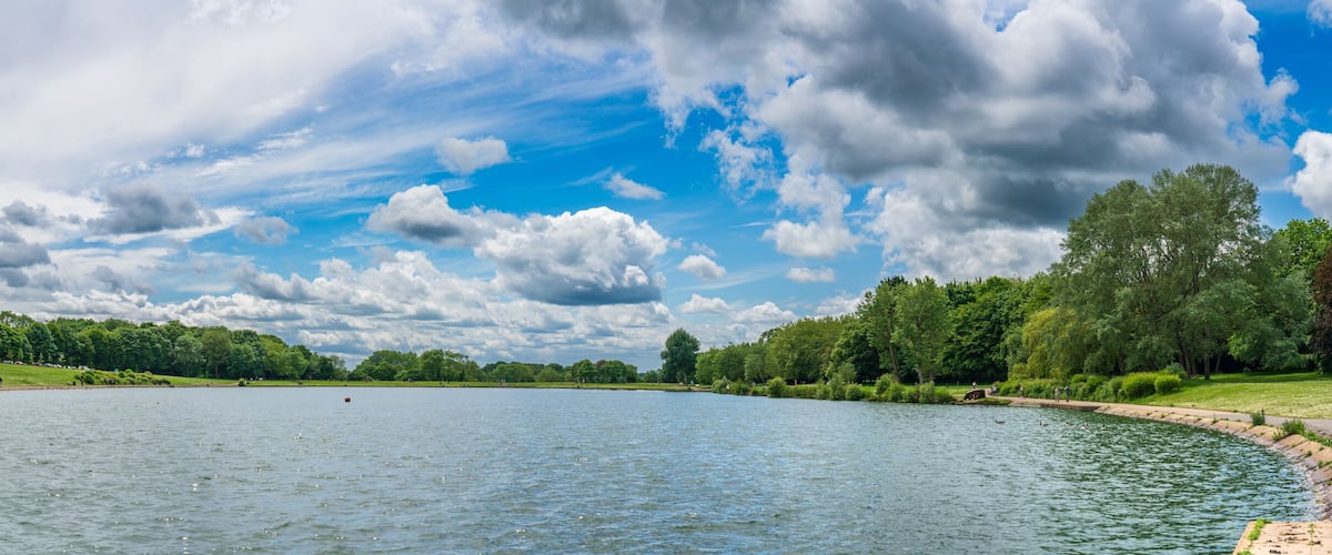 A calm lake surrounded by lush greenery and a partly cloudy sky.