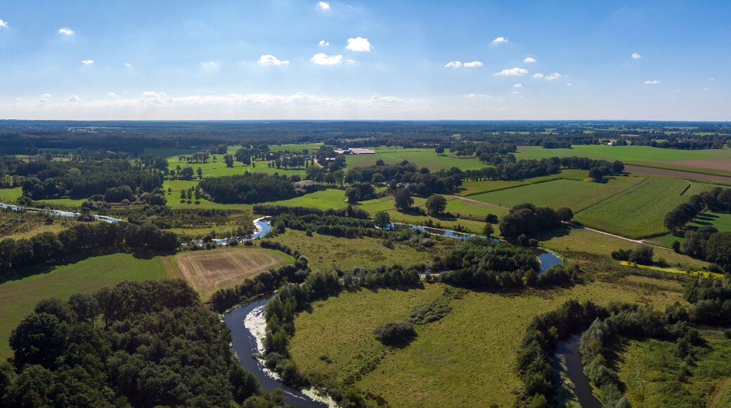 Wide aerial panorama of the river Regge meandering through the green Dutch Twente farmland landscape against a blue sky and clouds