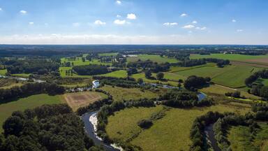 Wide aerial panorama of the river Regge meandering through the green Dutch Twente farmland landscape against a blue sky and clouds