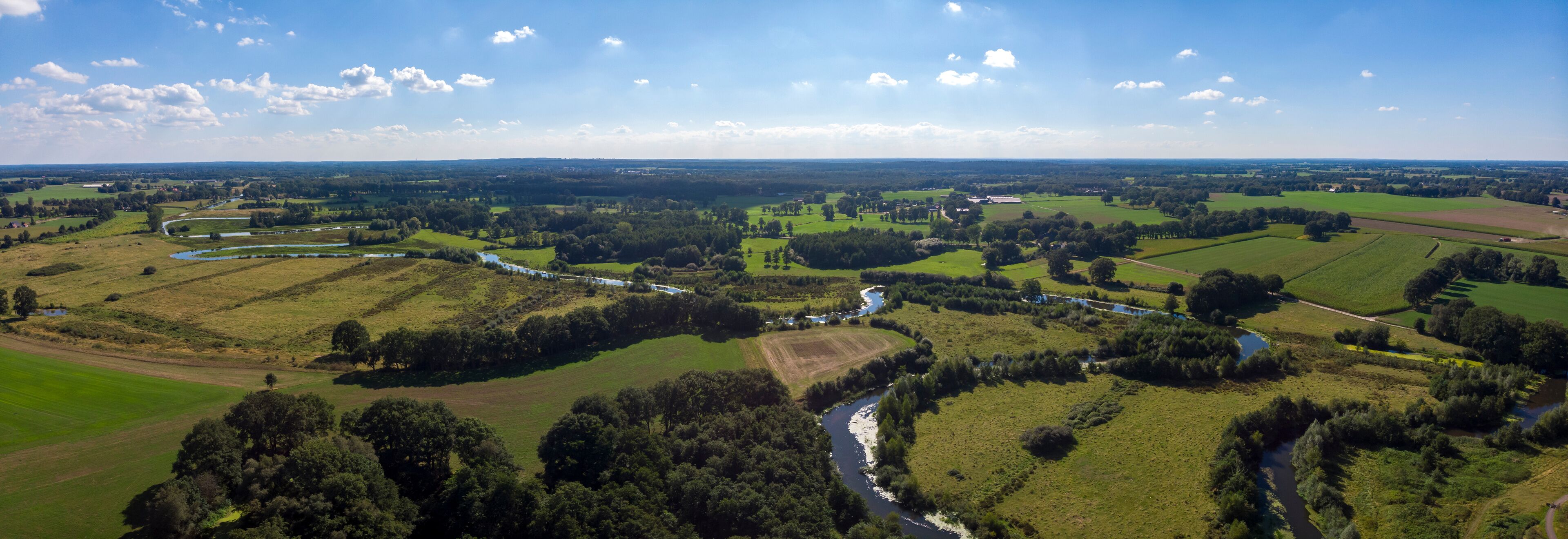 A river winding through green fields and forests, with scattered buildings and a distant horizon.