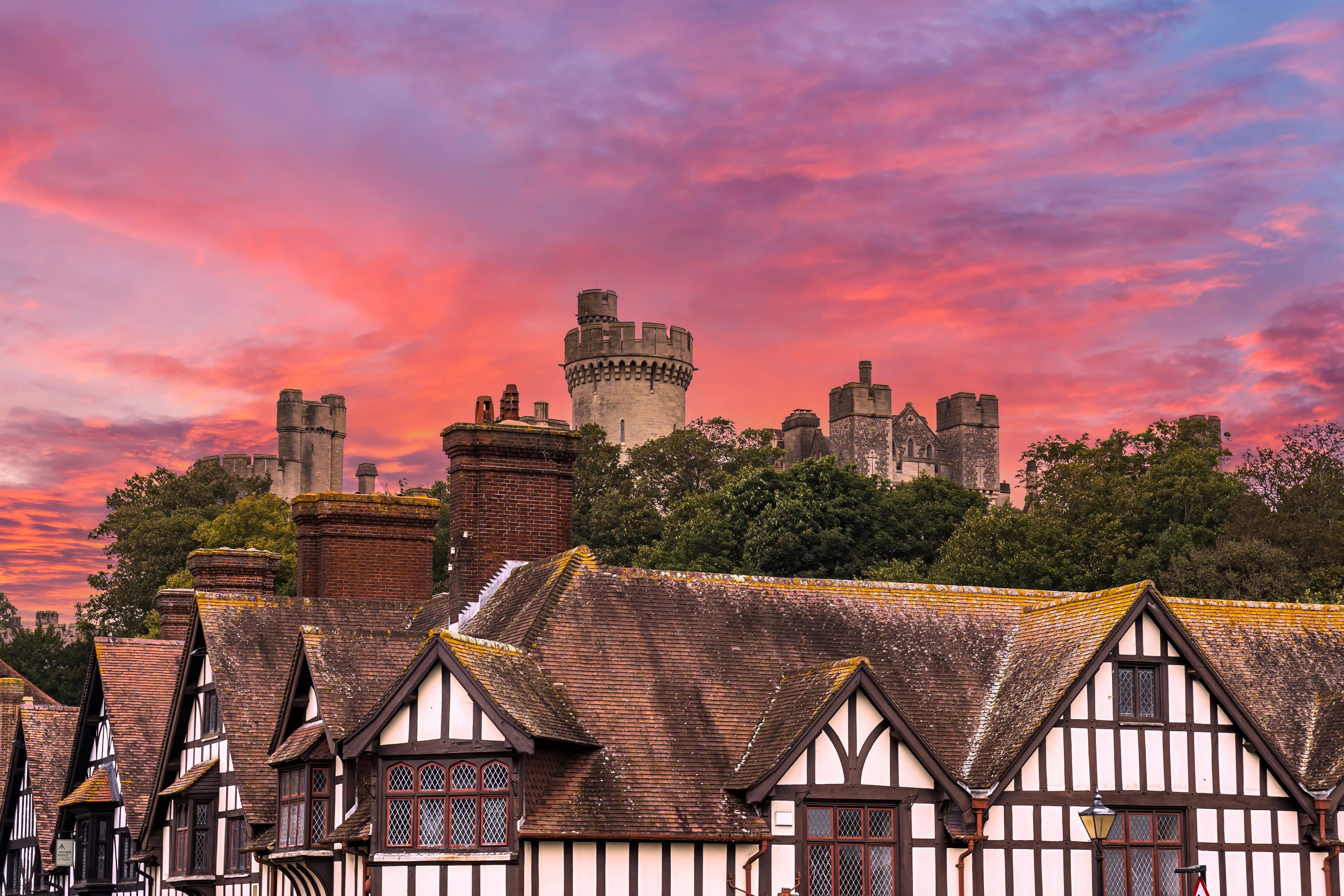 A historic castle with multiple towers and a traditional timber-framed building with a thatched roof.