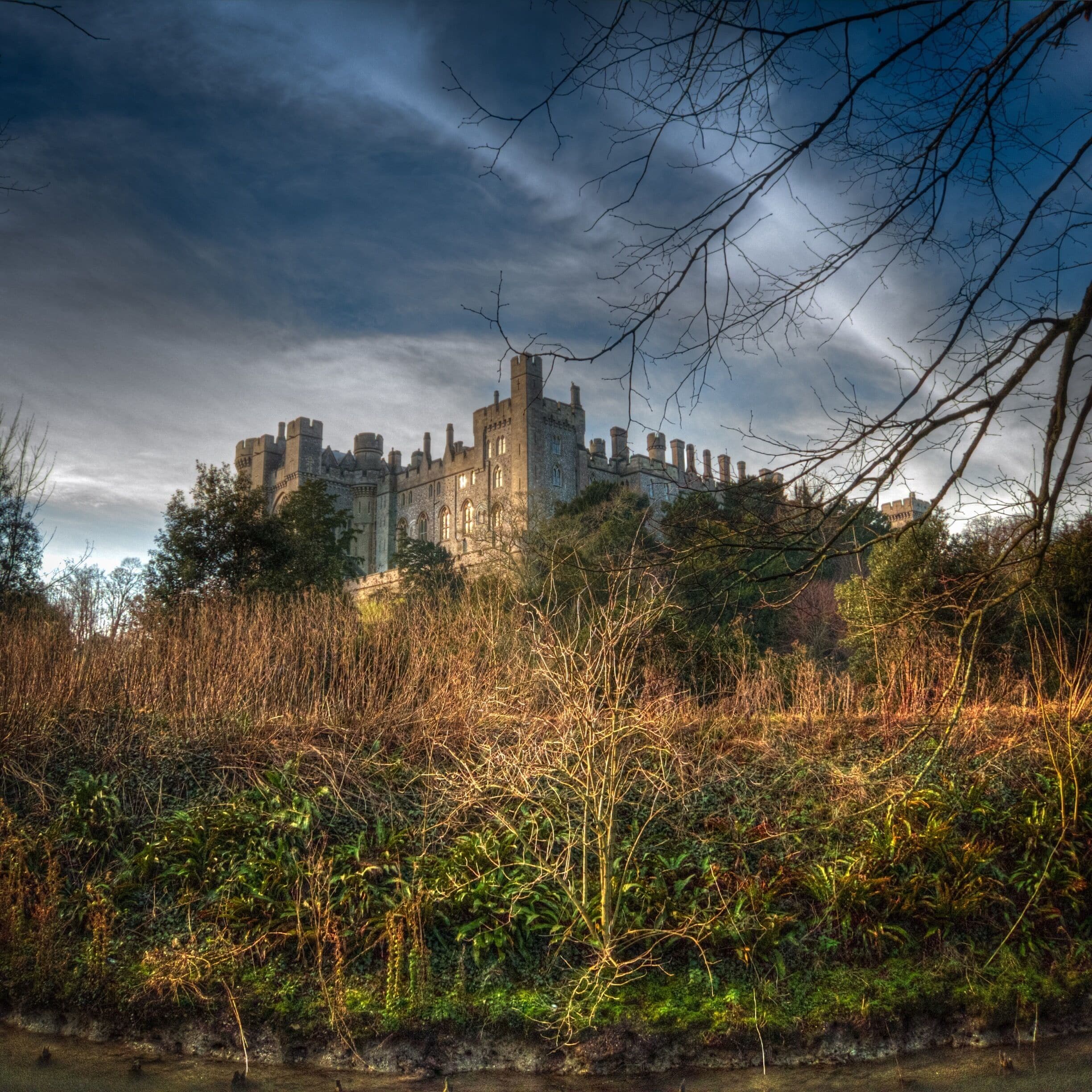 Un château médiéval entouré d’une végétation luxuriante, sous un ciel nuageux.