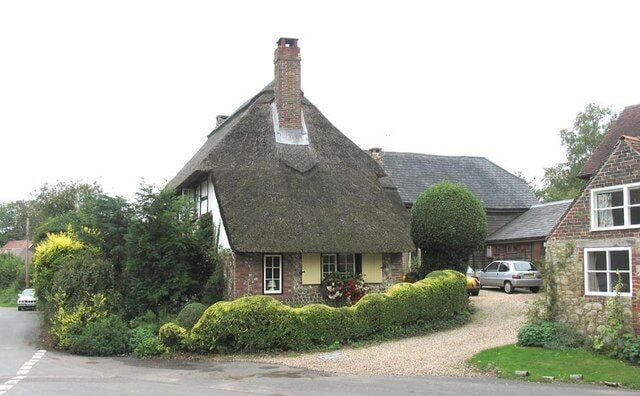 A traditional thatched-roof house with a gravel driveway and a well-kept garden.
