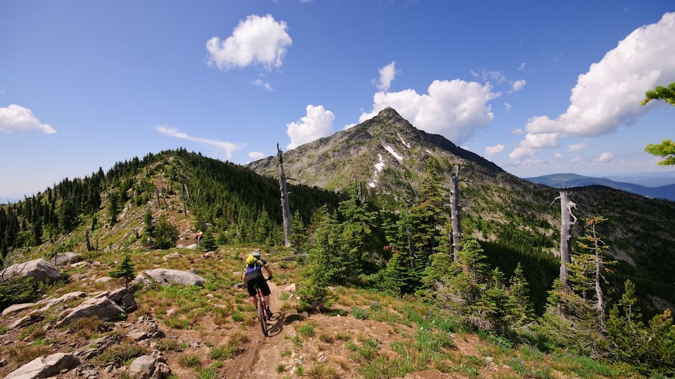 A mountain biker on a rocky trail with a snow-capped peak in the background.