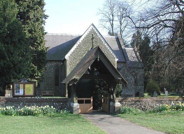A stone building with a triangular roof and a small porch. There is a pathway leading to the entrance, and a signboard is visible to the left.