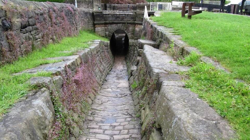 A stone pathway leading to a tunnel entrance, surrounded by stone walls and grass.