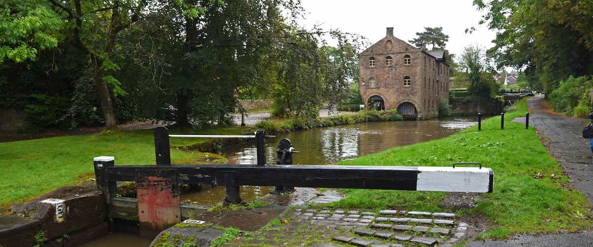 A canal with a lock gate, a brick building, and a grassy path.