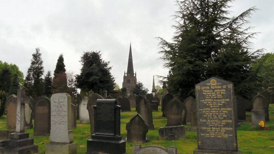 A cemetery with numerous headstones and a church spire in the background.
