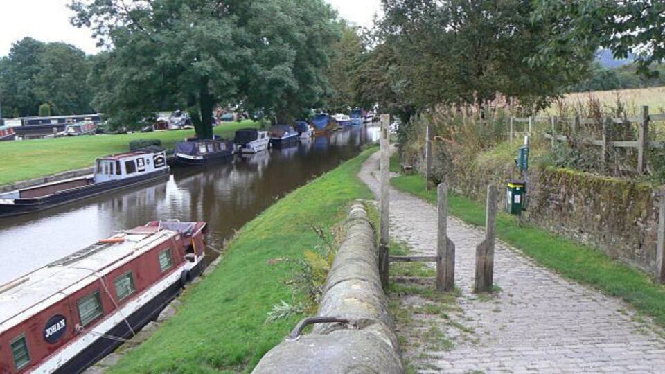 A canal with boats, a stone wall, a pathway, and trees.